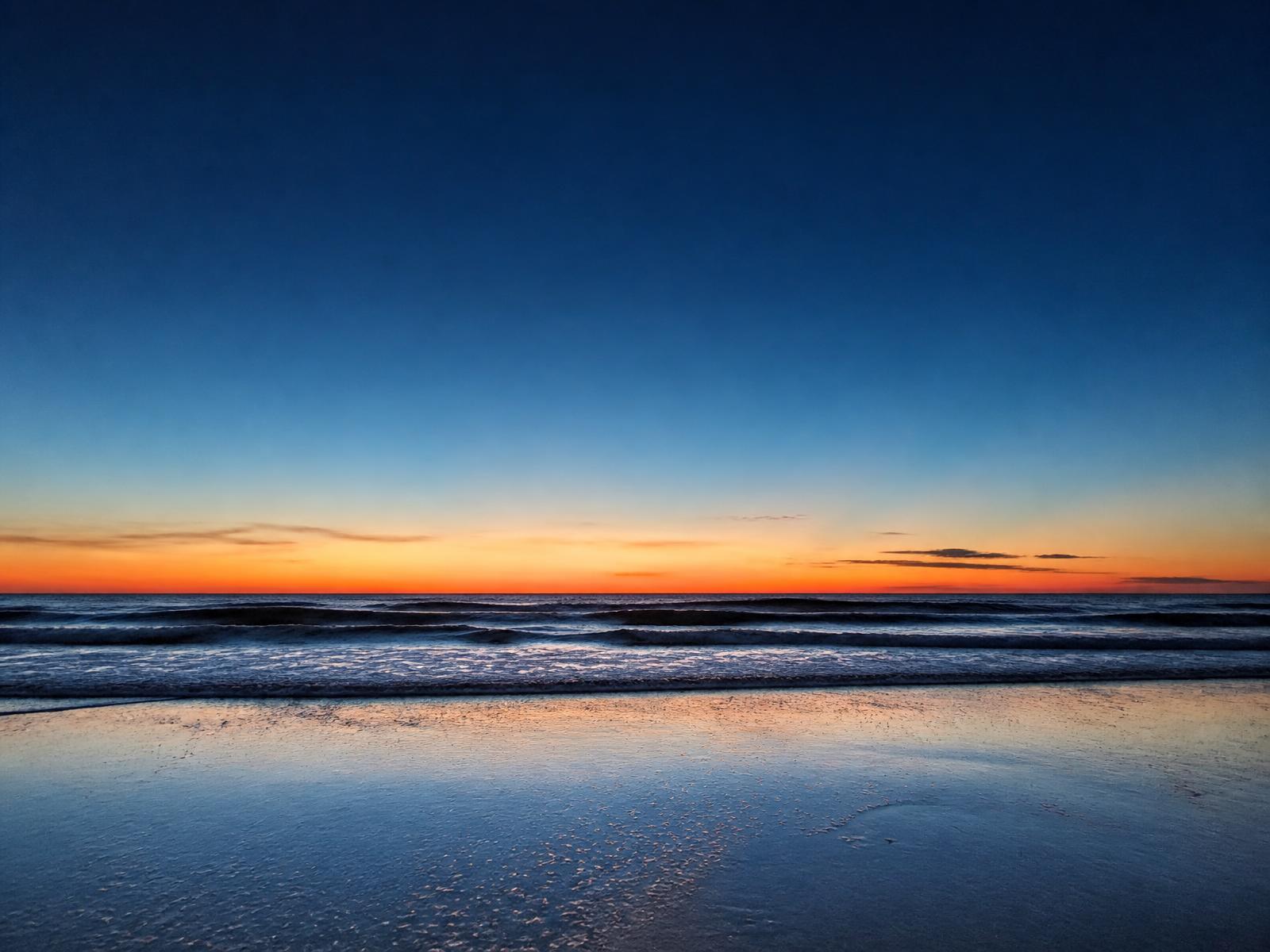 Open ocean beach at sunset with gentle waves and reflected light on wet sand